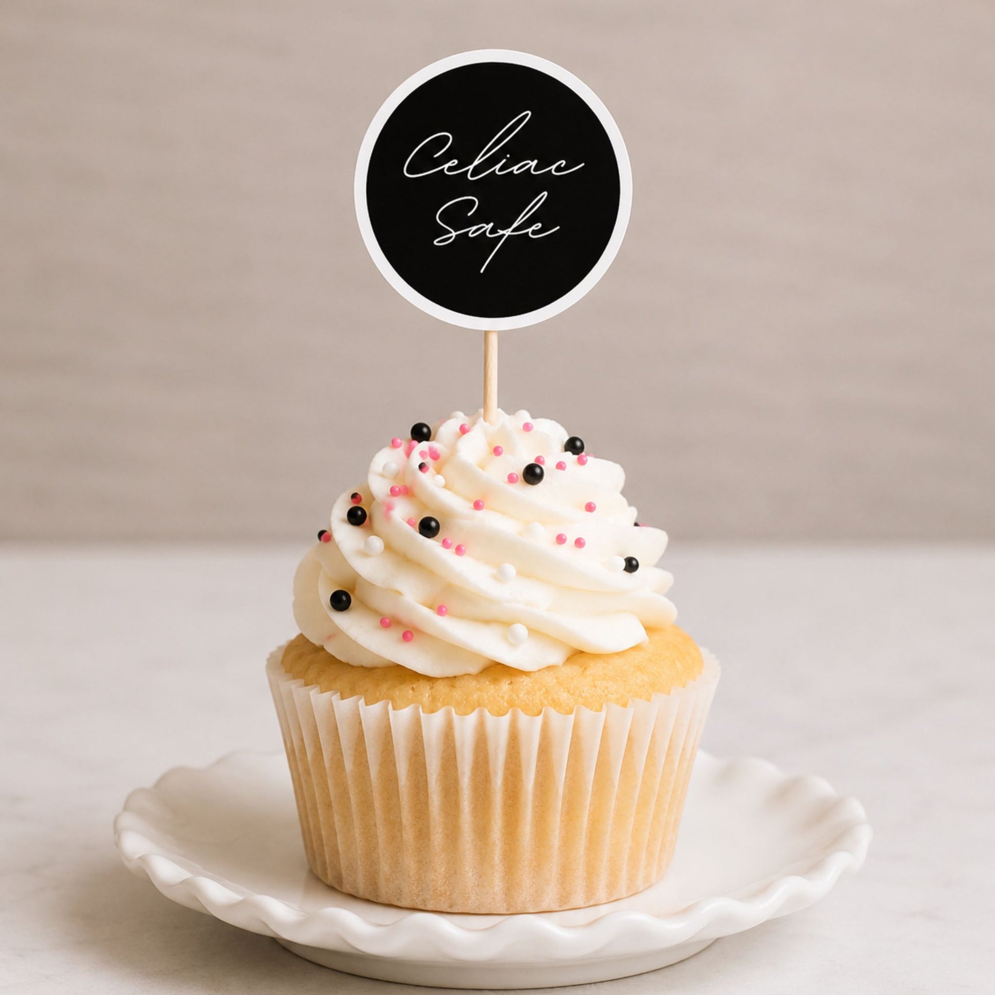 Black celiac safe label used as a cupcake topper on a frosted cupcake with sprinkles in a bright, minimal bakery-style setup.
