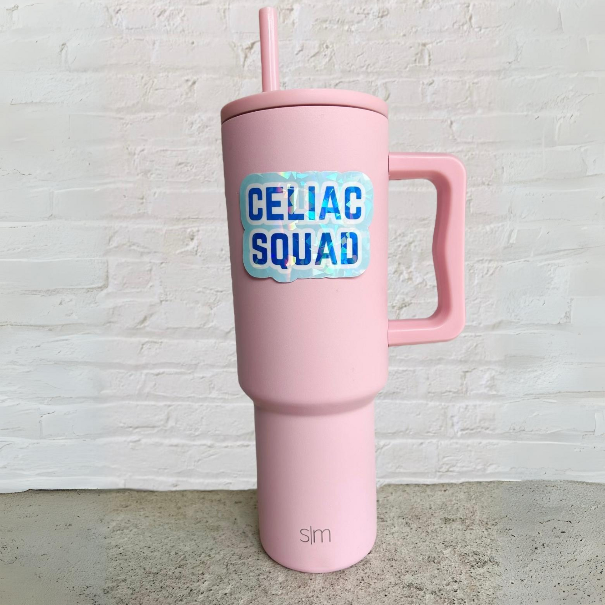Pink tumbler with a blue “Celiac Squad” sticker on the front.