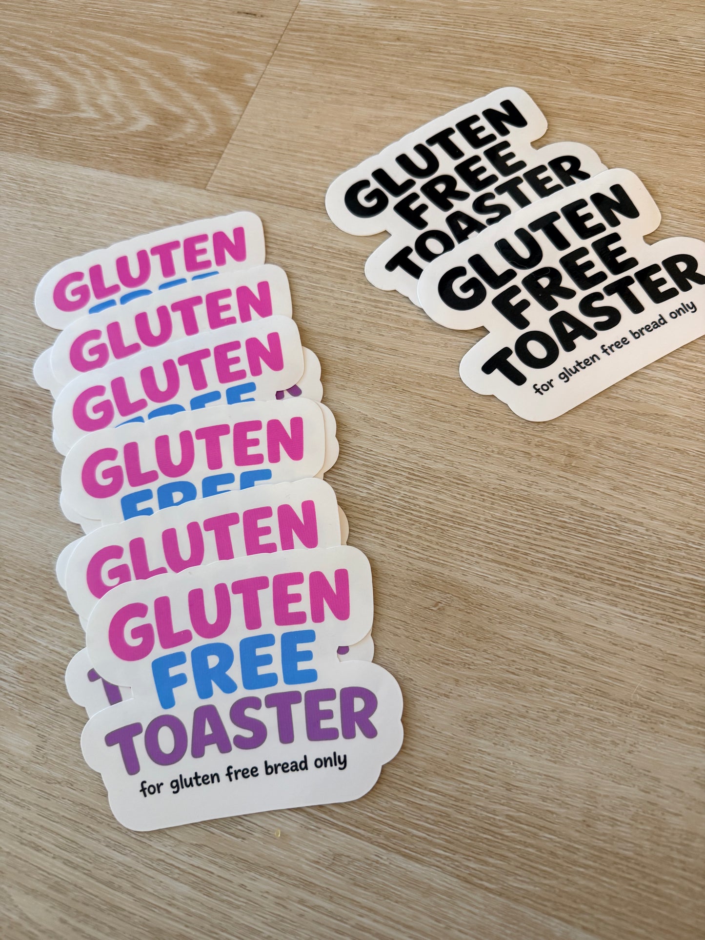 Pink and black Gluten Free Toaster stickers displayed on a wooden surface.